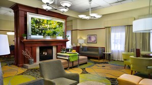 A hotel lobby with a fireplace, comfortable seating, a large TV screen, and a carpeted floor. - Hilton Garden Inn Detroit Downtown (Detroit)
