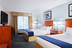 Two single beds with white linens and blue bedspreads, a nightstand, and a television are featured in this hotel room.