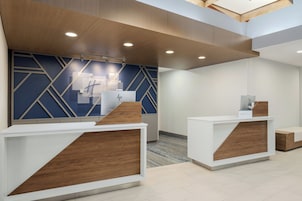 Uma área de recepção com design moderno, destacando um balcão de atendimento, uma parede com padrões geométricos e iluminação embutida no teto.