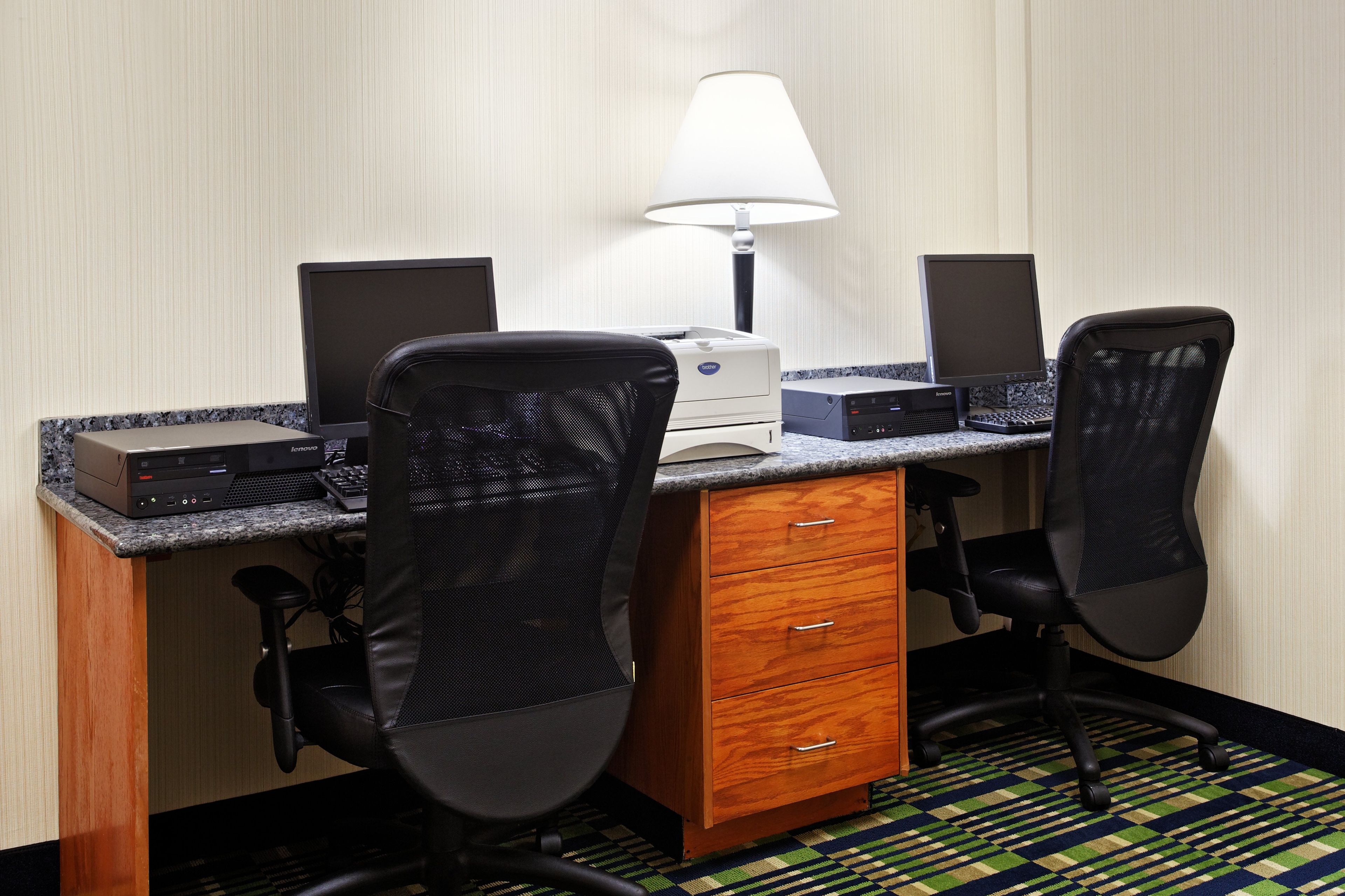 A hotel room with a desk, two chairs, a lamp, and a printer.