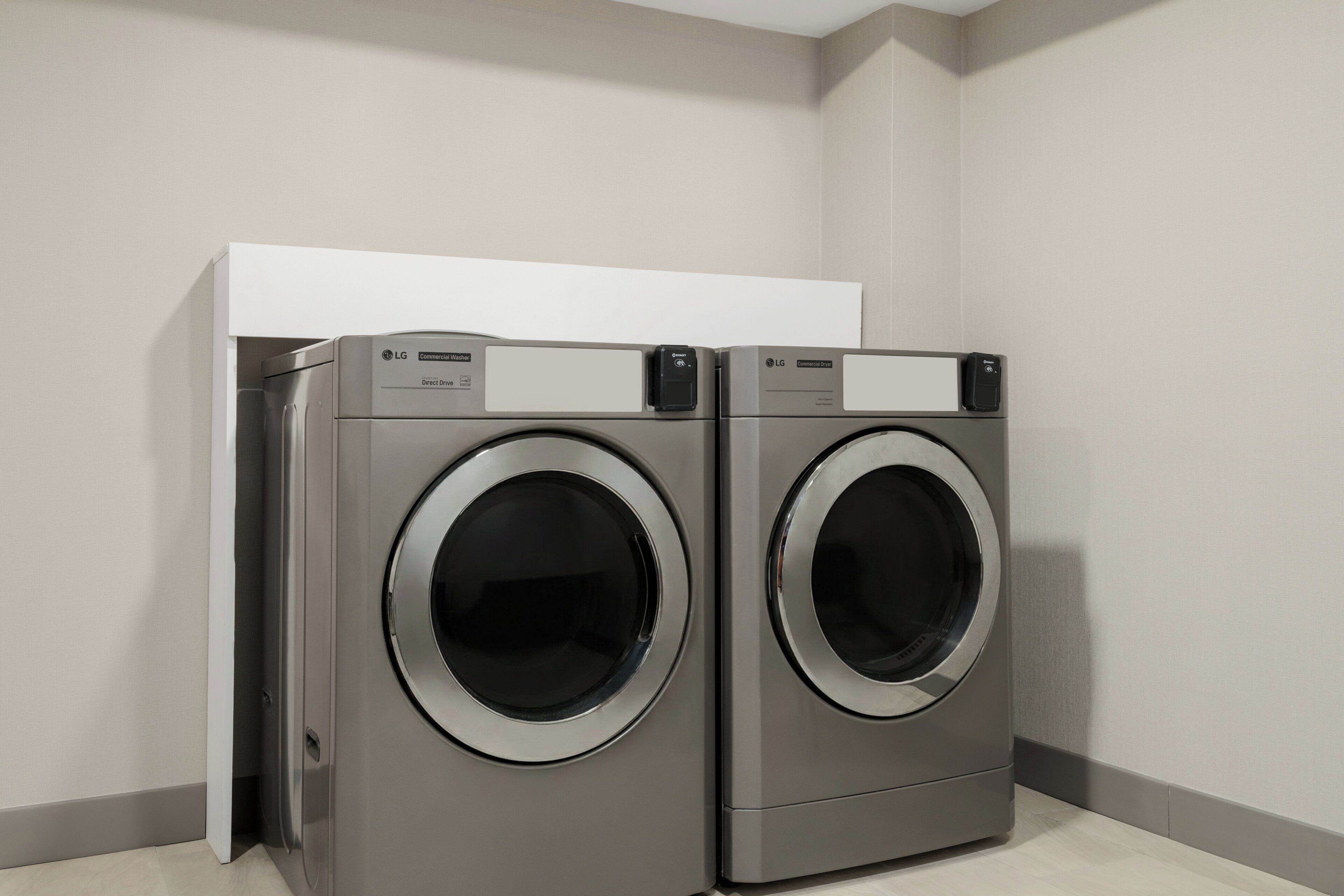 Two LG Direct Drive front-loading washing machines in a corner of a room with a white cabinet above them.