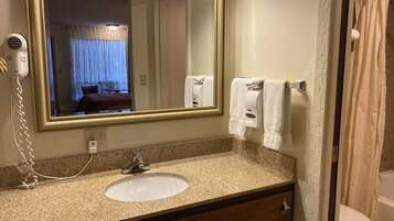 A bathroom with a granite countertop sink, a mirror, a hairdryer, and a towel dispenser.