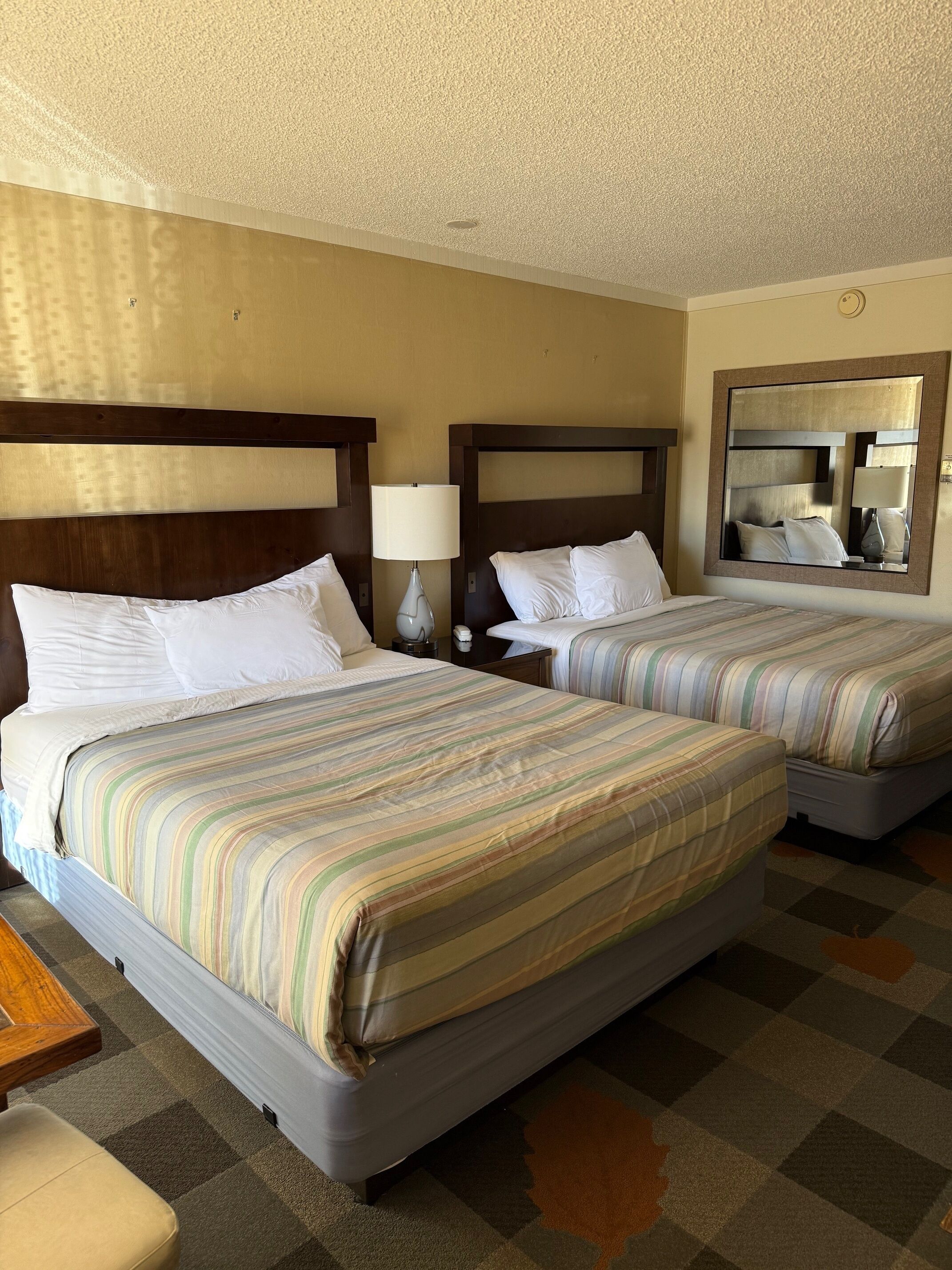 Una habitación de hotel con dos camas, un espejo grande y un cabecero de madera.