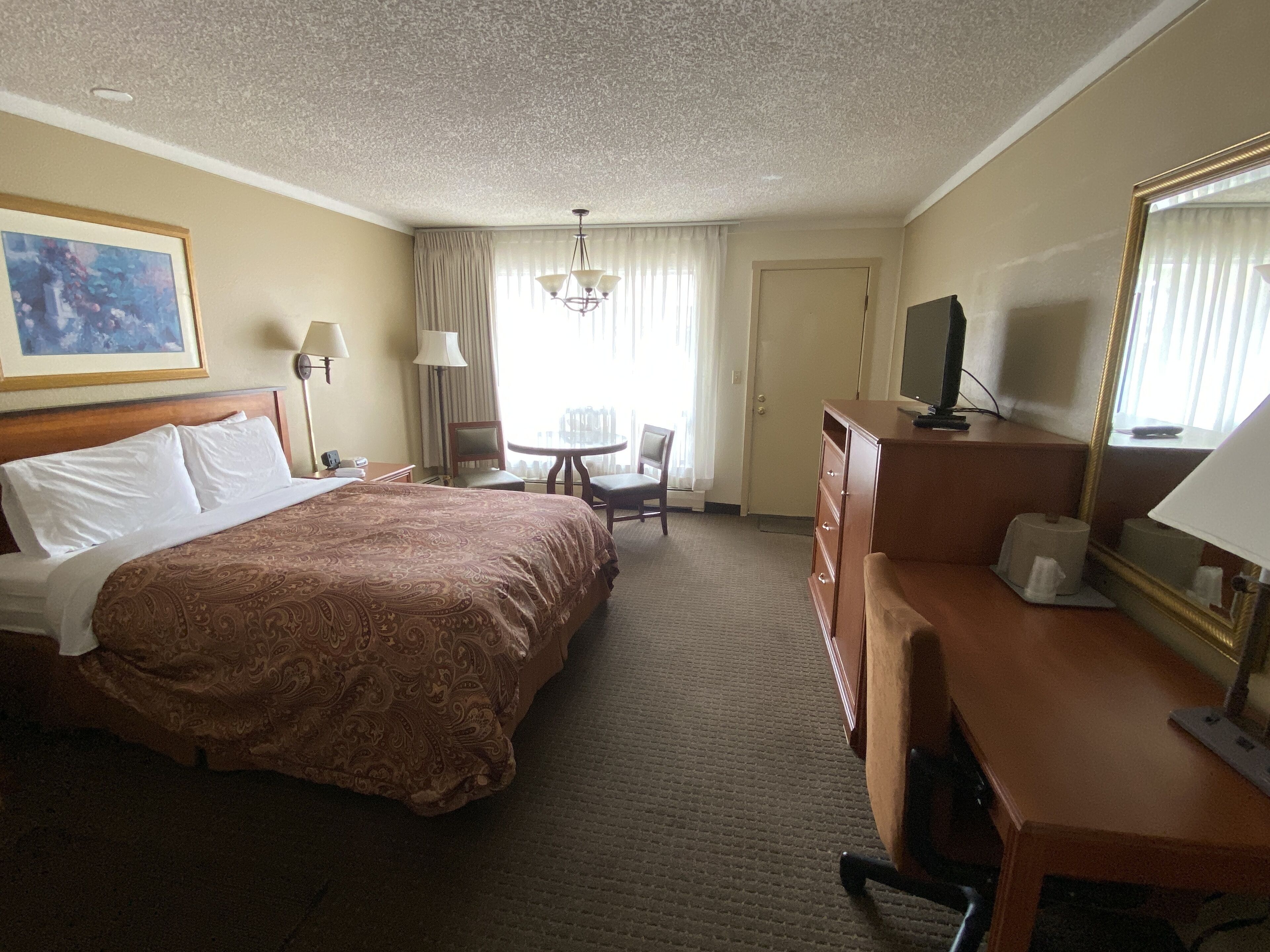 Una camera d'albergo con un letto grande, una scrivania con sedia, una televisione e uno specchio.