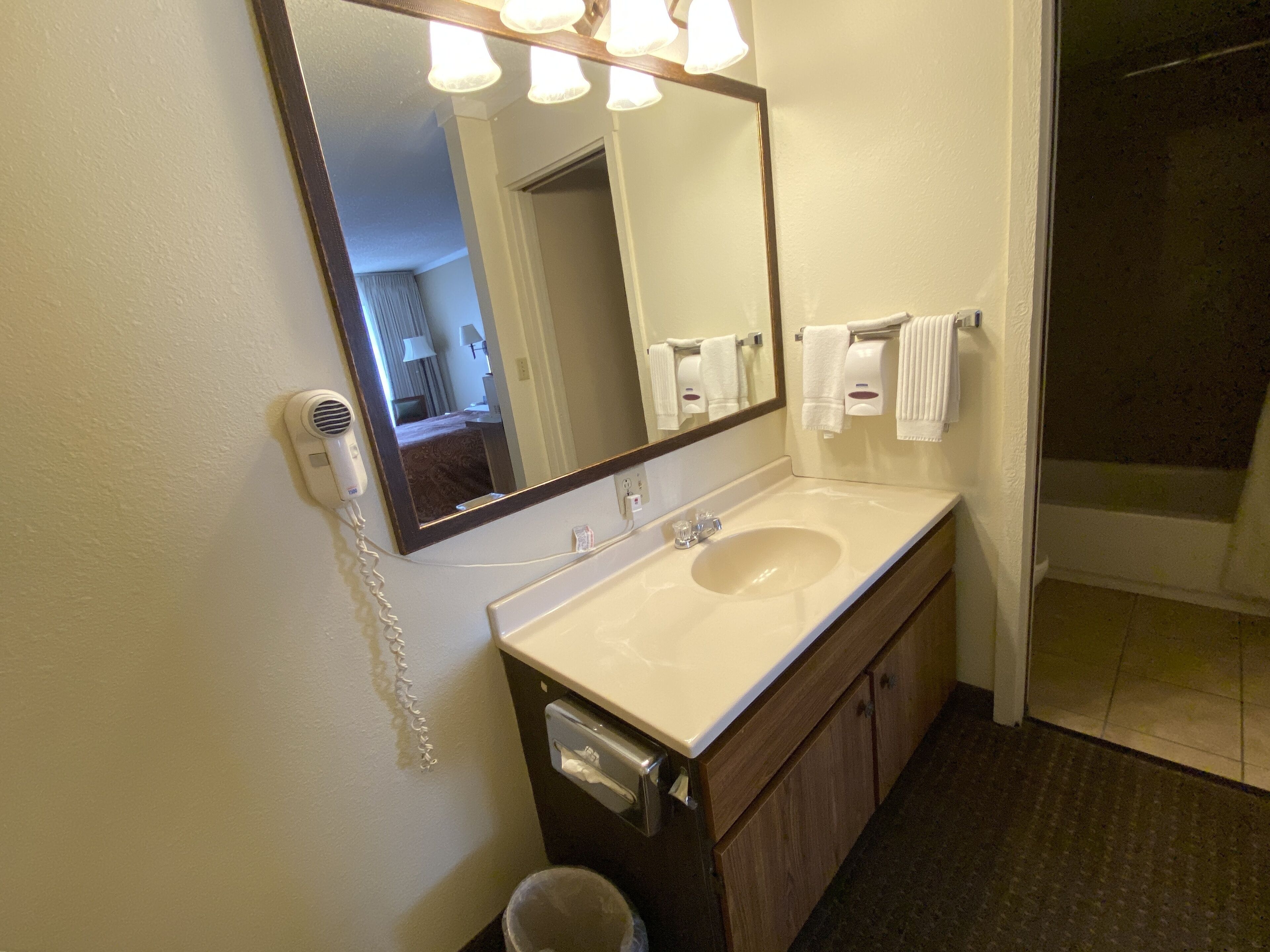 A bathroom with a large mirror, a sink, a towel dispenser, and a hairdryer.