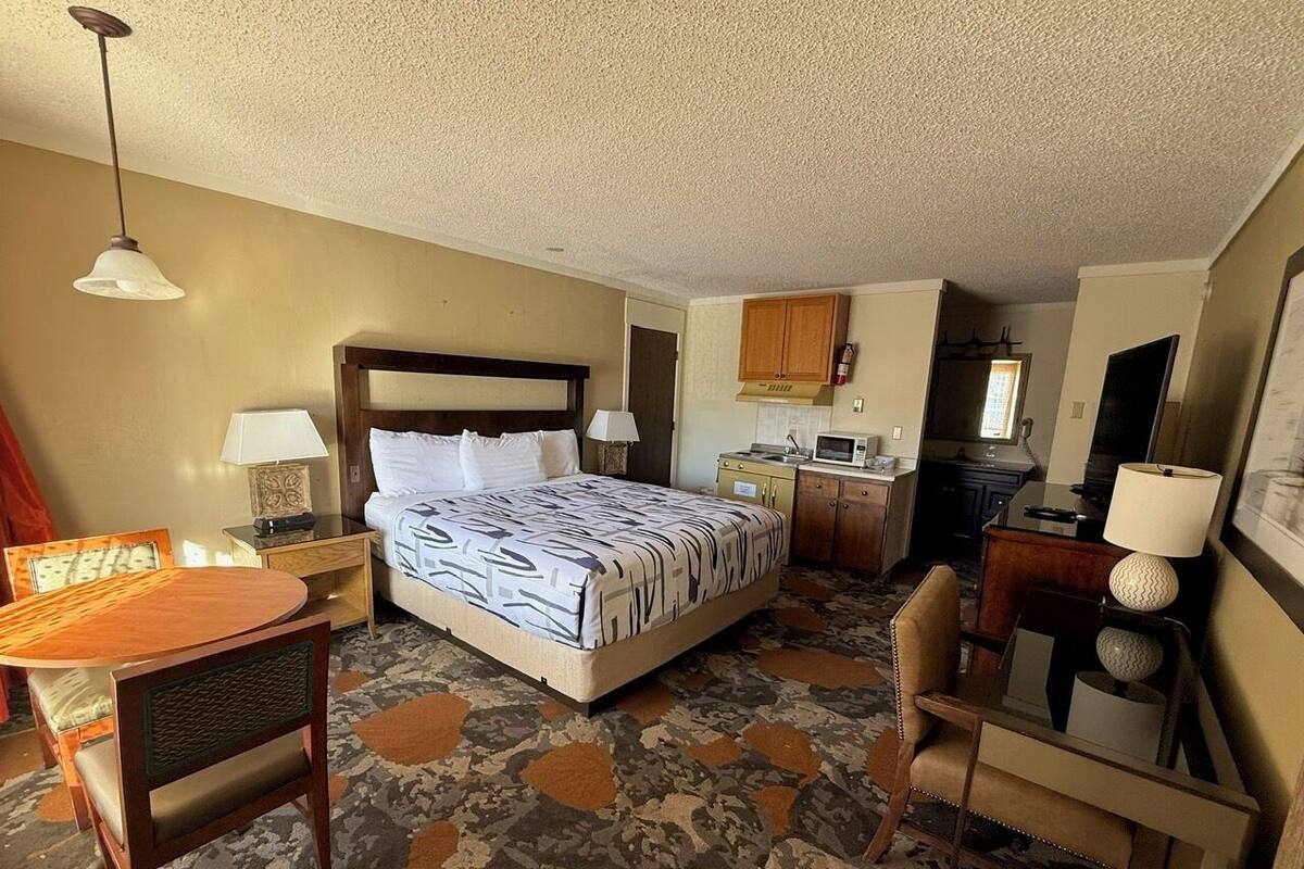 A hotel room with a bed, a desk, a chair, a lamp, and a television.
