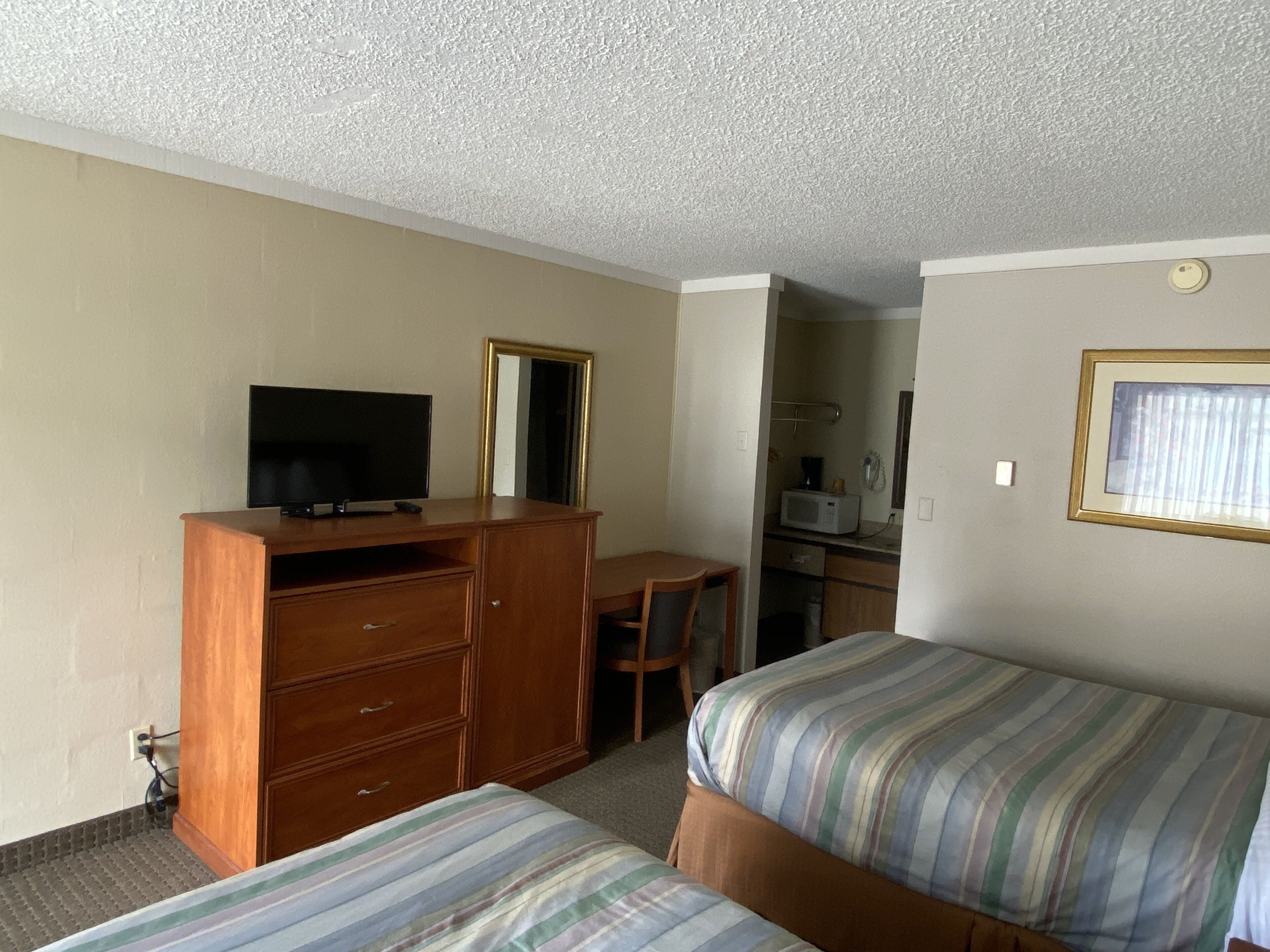 A hotel room with two single beds, a wooden dresser with a television, a desk, and a mirror.