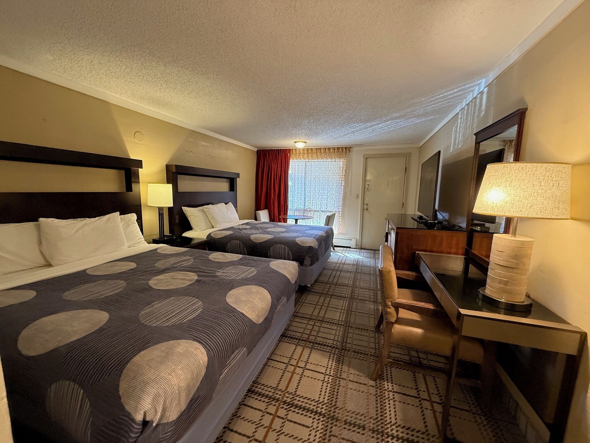 A hotel room with two beds, a desk, a chair, a TV, and a window with curtains.