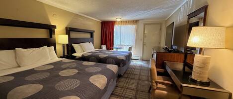 A hotel room with two beds, a desk, a chair, a TV, and a window with curtains.