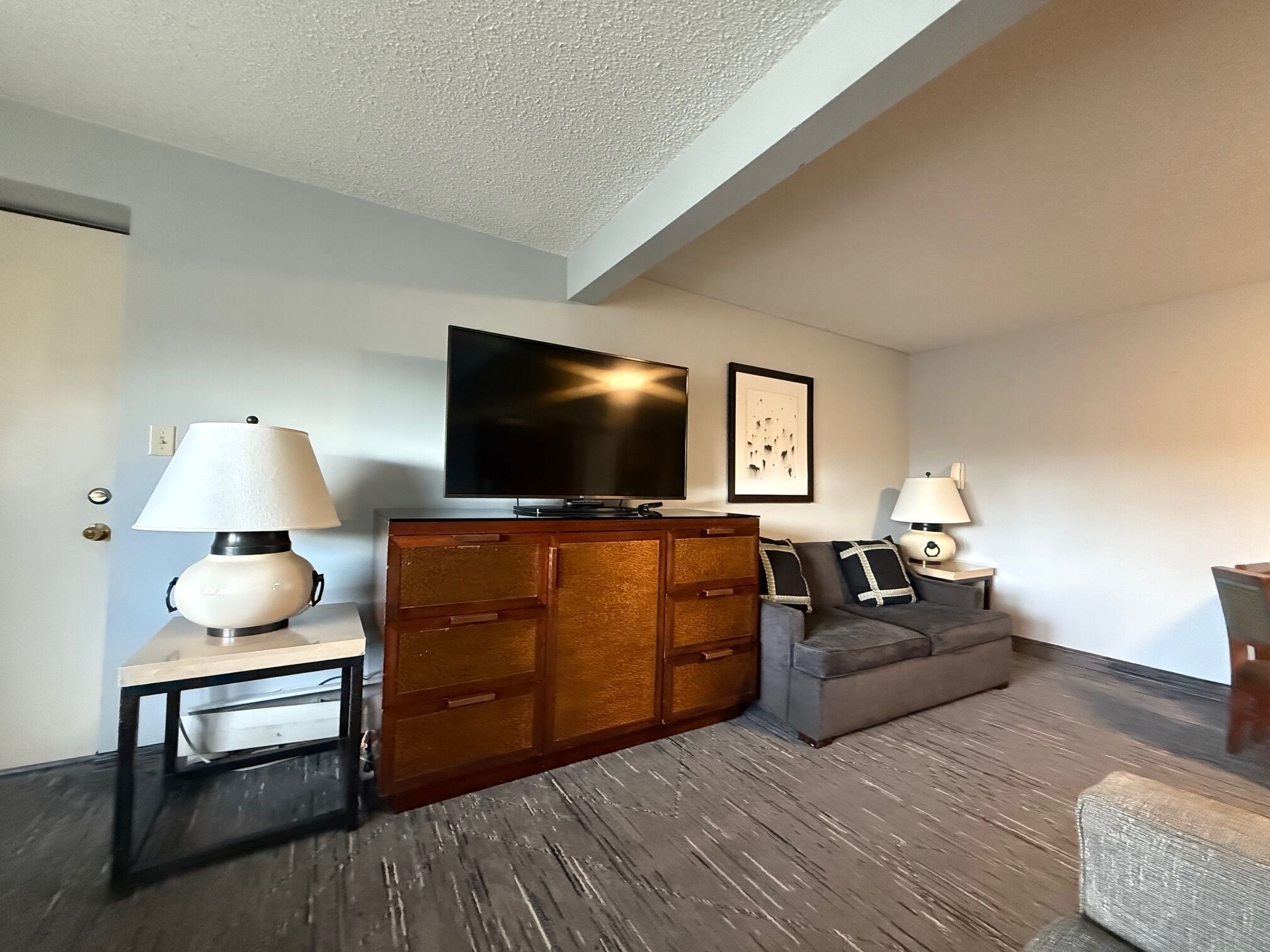 A modern living room with a flat-screen TV, wooden cabinet, grey sofa, and two side tables with lamps.