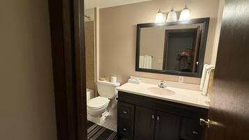A bathroom with a toilet, sink, mirror, and dark cabinets.