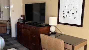 Habitación de hotel con una cama, un escritorio con una silla, un televisor, una lámpara y un cuadro en la pared.