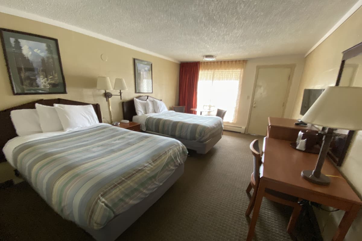 A hotel room with two beds, a desk, a chair, a lamp, a telephone, and a window with curtains.