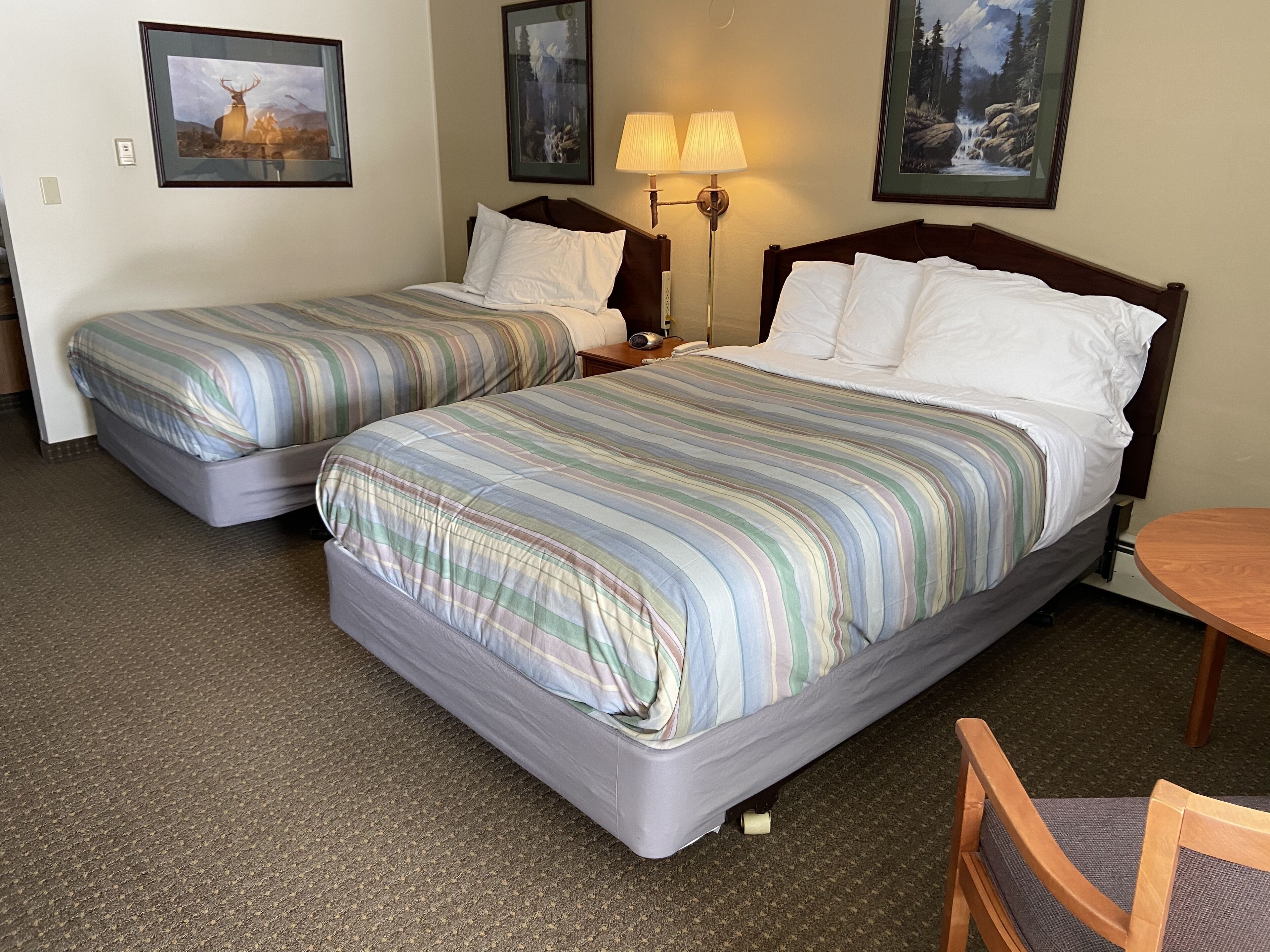 Two single beds with striped bedding, a nightstand with a lamp, and framed pictures on the wall.