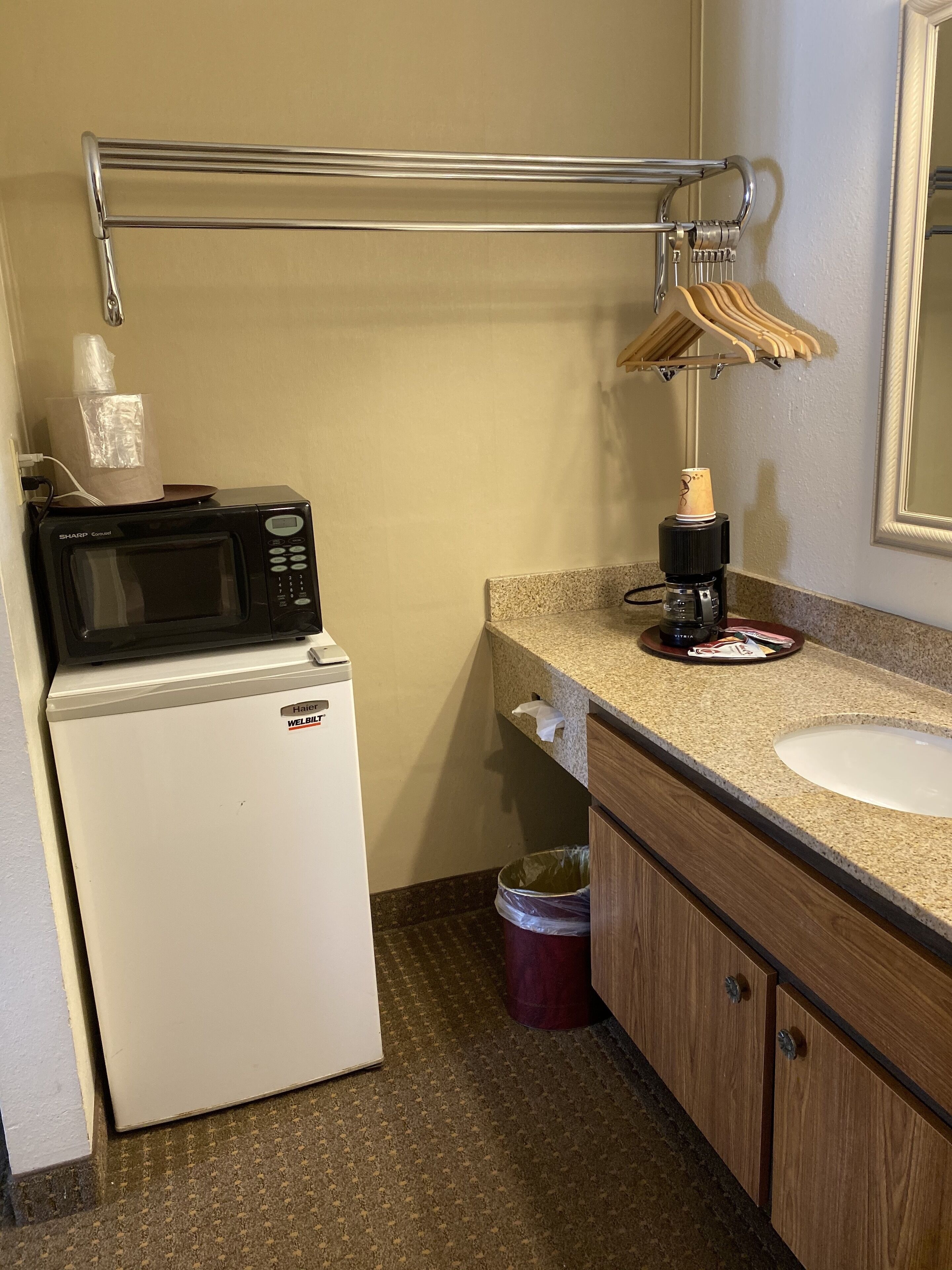 A compact bathroom with a white refrigerator, a coffee maker, a sink, and a towel rack.