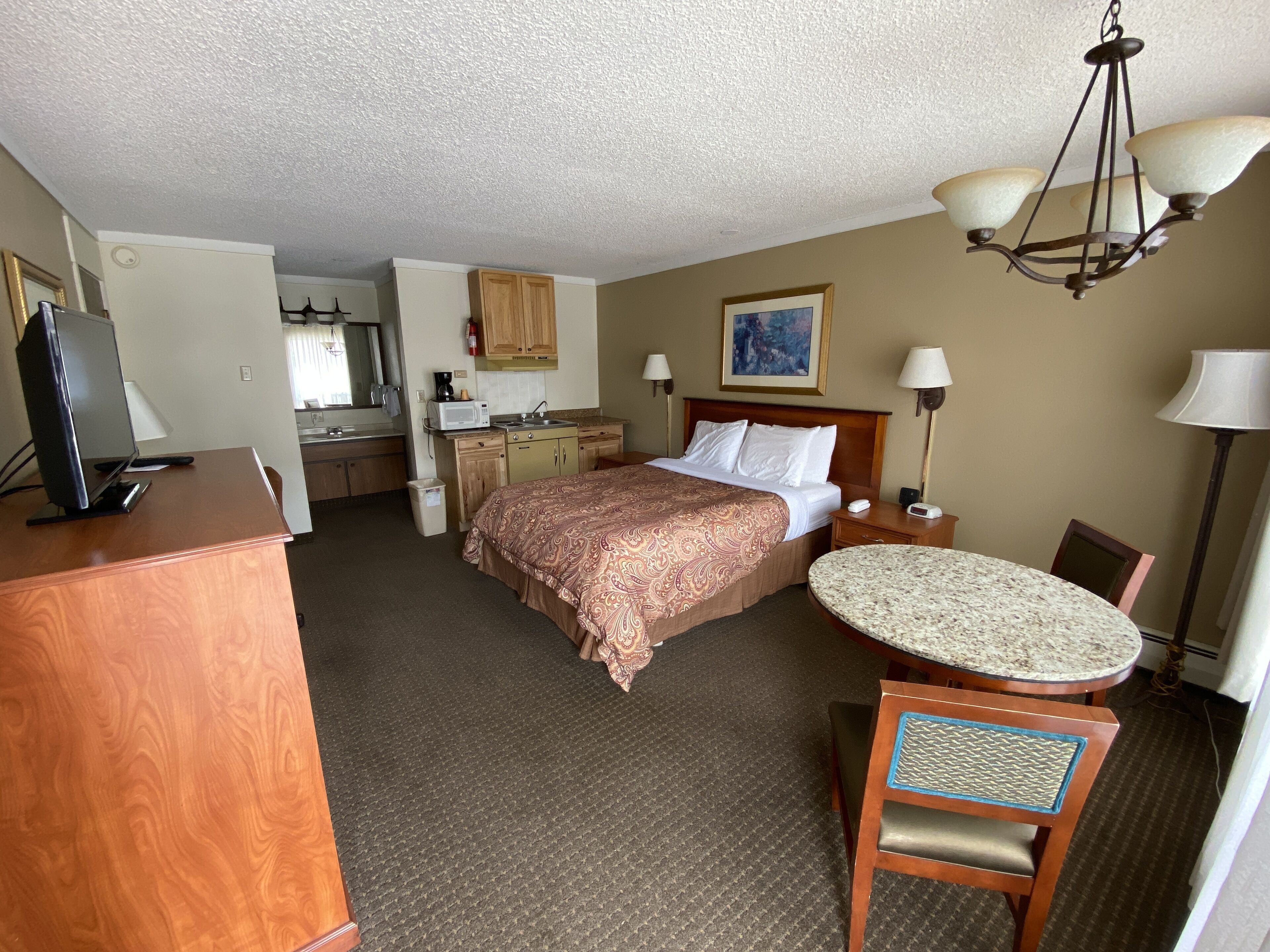 A hotel room with a bed, desk, chair, and a small dining table.