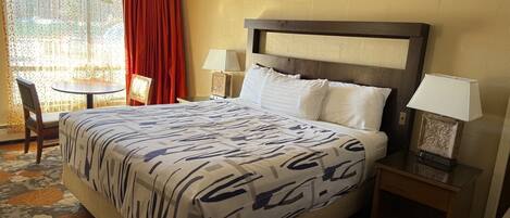 A hotel room with a large bed, two bedside tables, a chair, a small table, and a window with curtains.