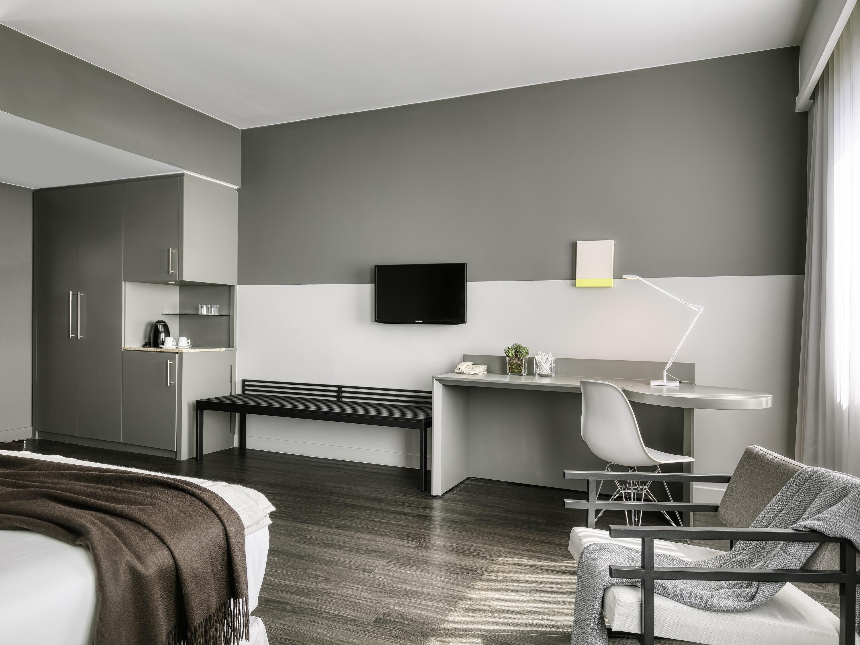 Habitación de hotel moderna con cama, escritorio, silla, televisión y ventana.