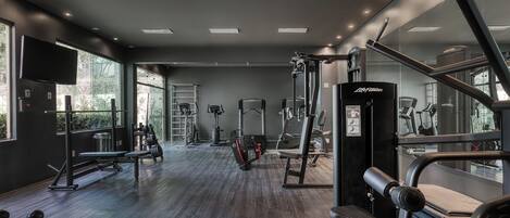 Un gimnasio moderno con diversos equipos de ejercicio, ventanas amplias y un muro con espejos.