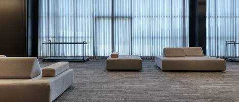 A modern hotel room with a large window, a sofa, a small table, and a standing lamp.