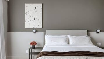 A modern bedroom with a large bed, a nightstand, a wall-mounted light, and a piece of abstract art.
