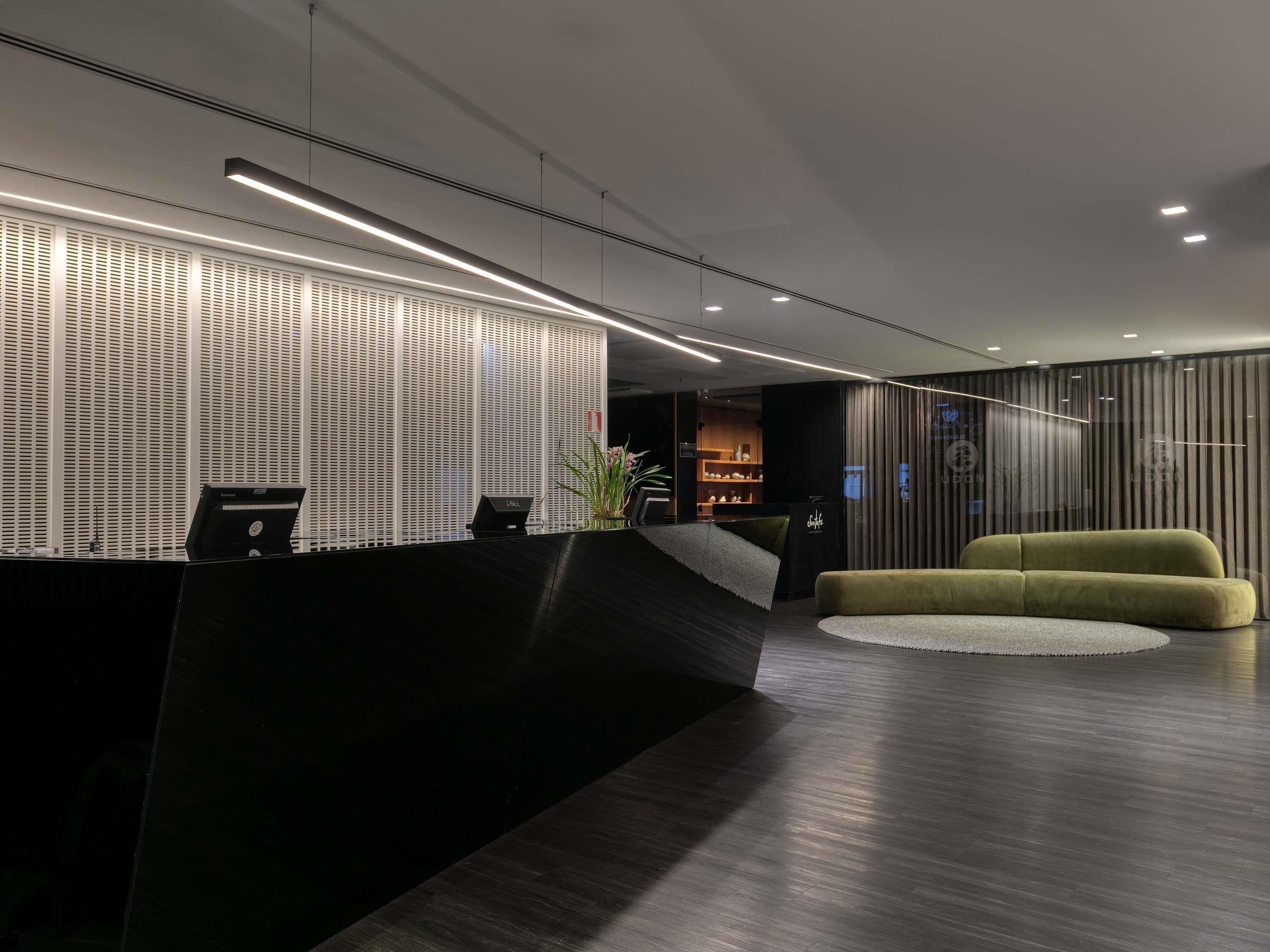 A modern reception area with a black reception desk, a green sofa, and a patterned wall.