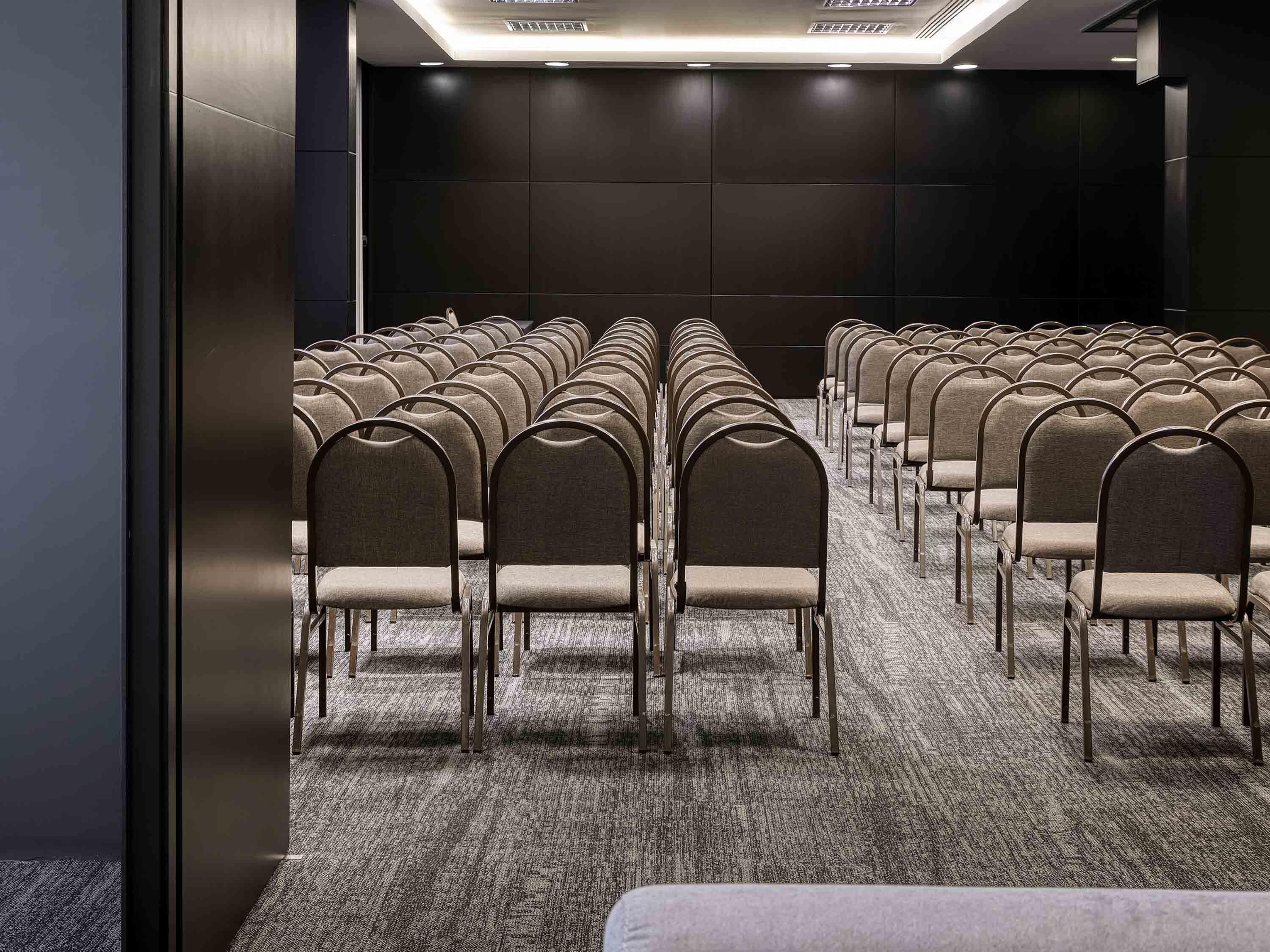A conference room with rows of chairs, carpeted floor, and dark walls.