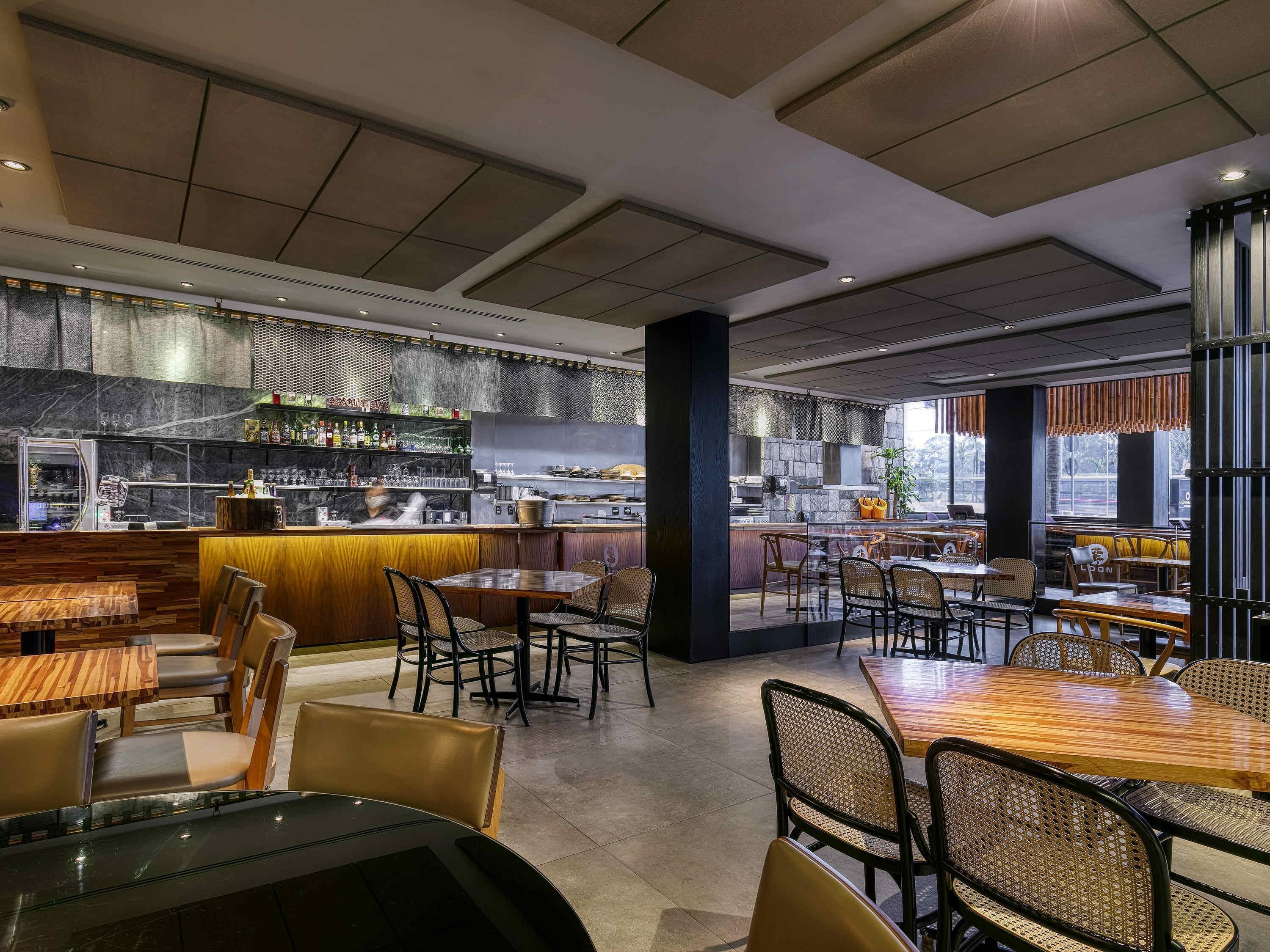 A modern restaurant interior with a bar area, seating arrangements, and a view of the kitchen.