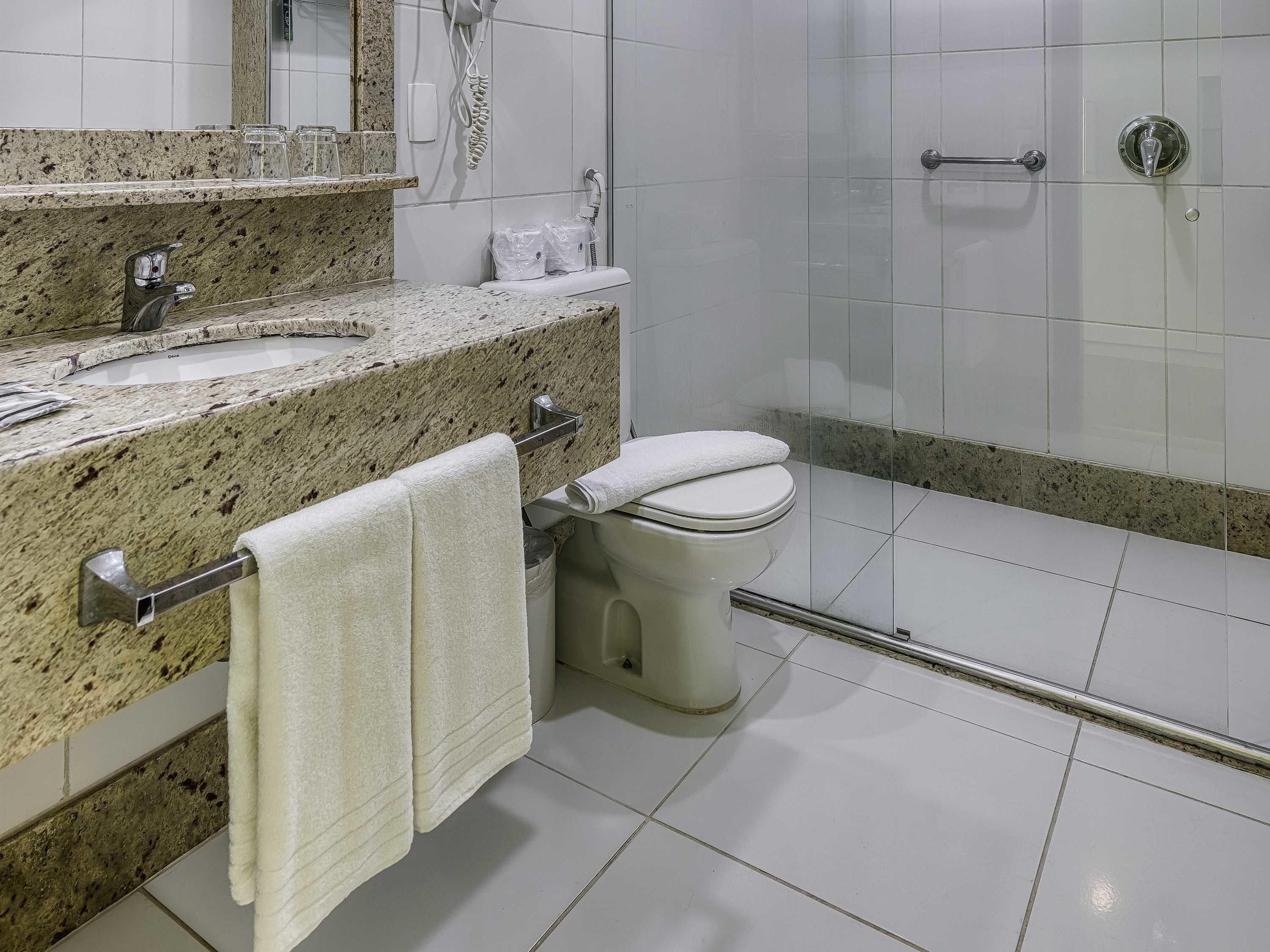 Une salle de bain moderne dotée d’un comptoir en granit, de toilettes, d’un espace douche et d’une cabine de douche en verre.