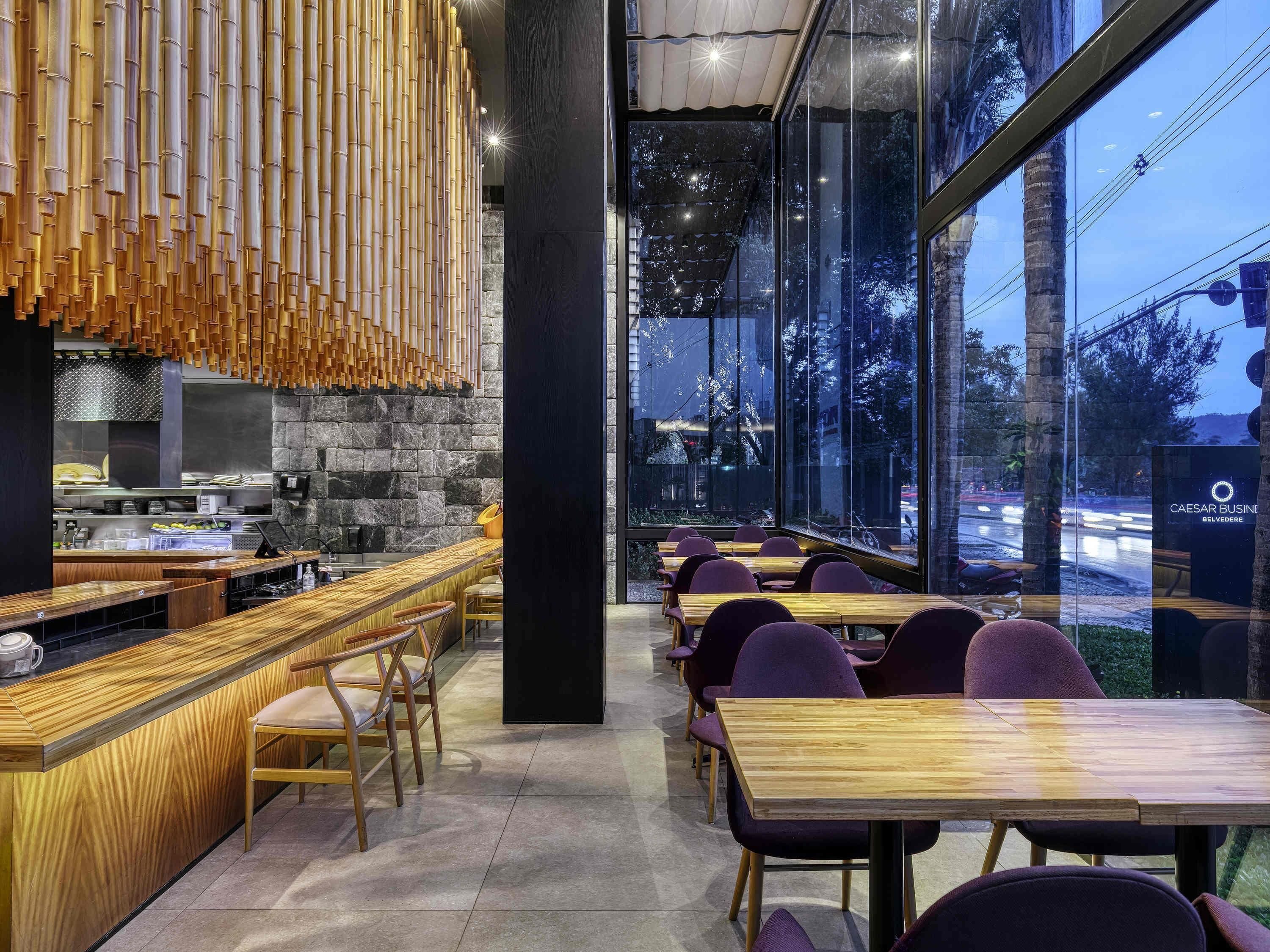 Interior de un restaurante moderno con barra, asientos y amplios ventanales que dan a la calle.