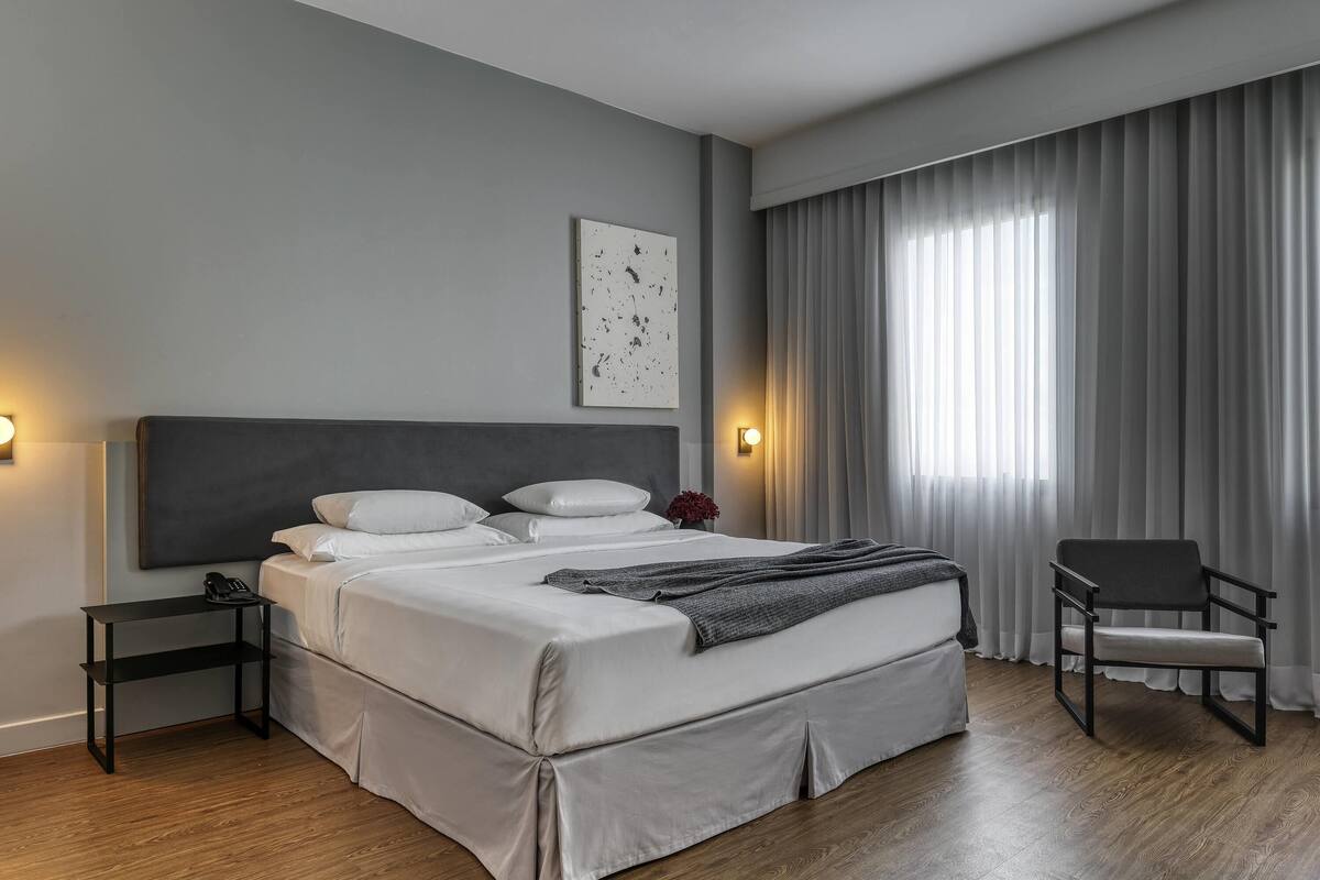 Ein modernes Hotelzimmer mit einem großen Bett, Nachttischen, einem Sessel und Blick ins Freie.
