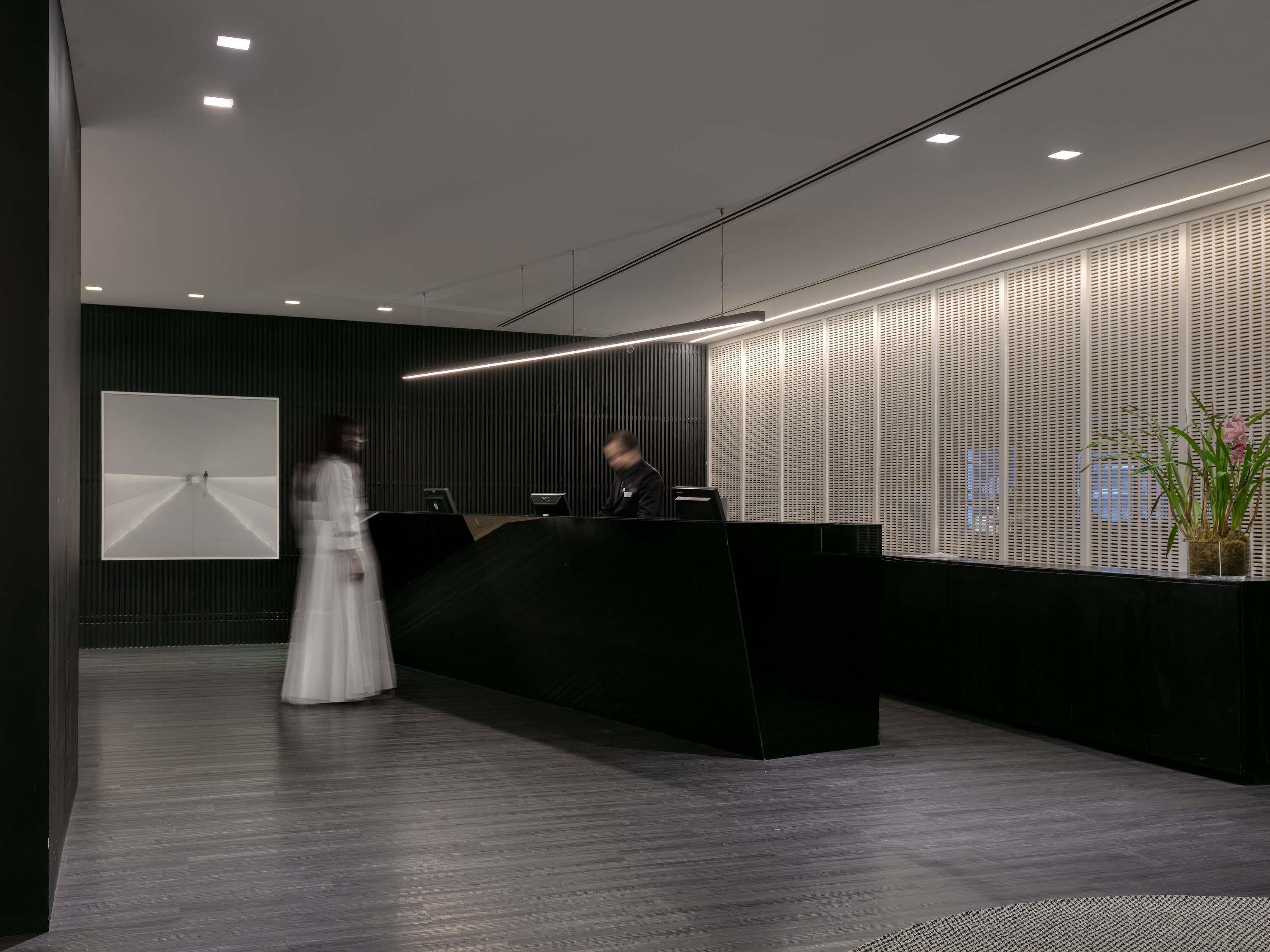 A modern reception area with a dark reception desk, a large framed artwork on the wall, and a potted plant.