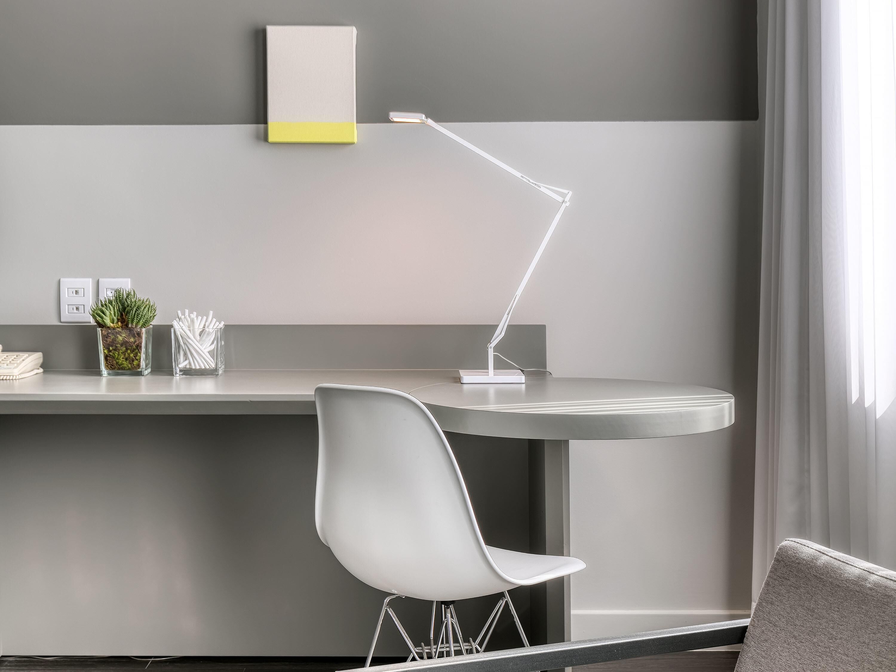 A modern workspace with a desk, chair, desk lamp, and a small potted plant.