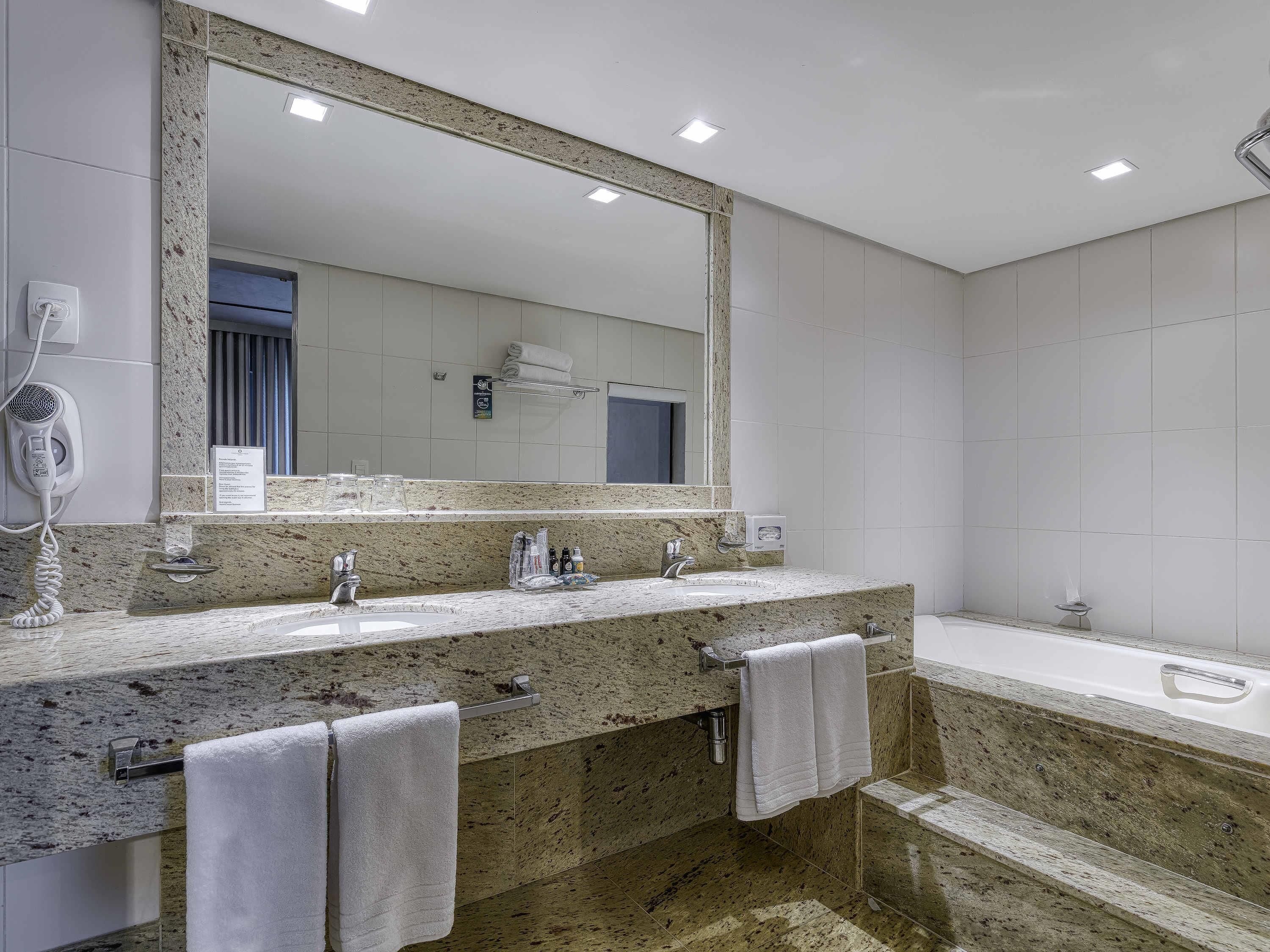 A modern bathroom with a granite countertop, two sinks, a large mirror, and a bathtub.