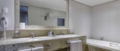 A modern bathroom with a granite countertop, two sinks, a large mirror, and a bathtub.