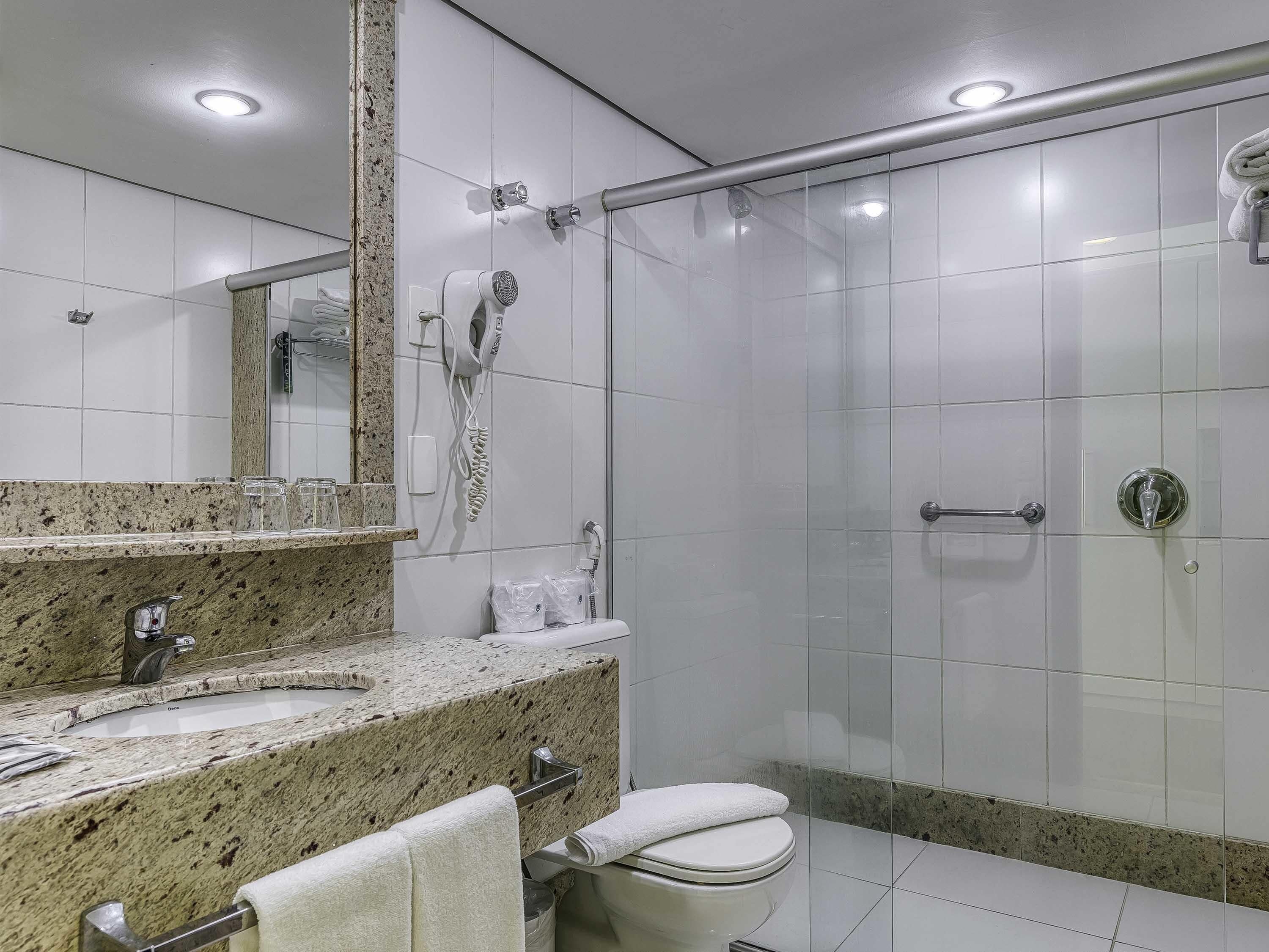 Een moderne badkamer met een granieten aanrechtblad, een toilet, een douche met glazen deur en een handdoekhouder.