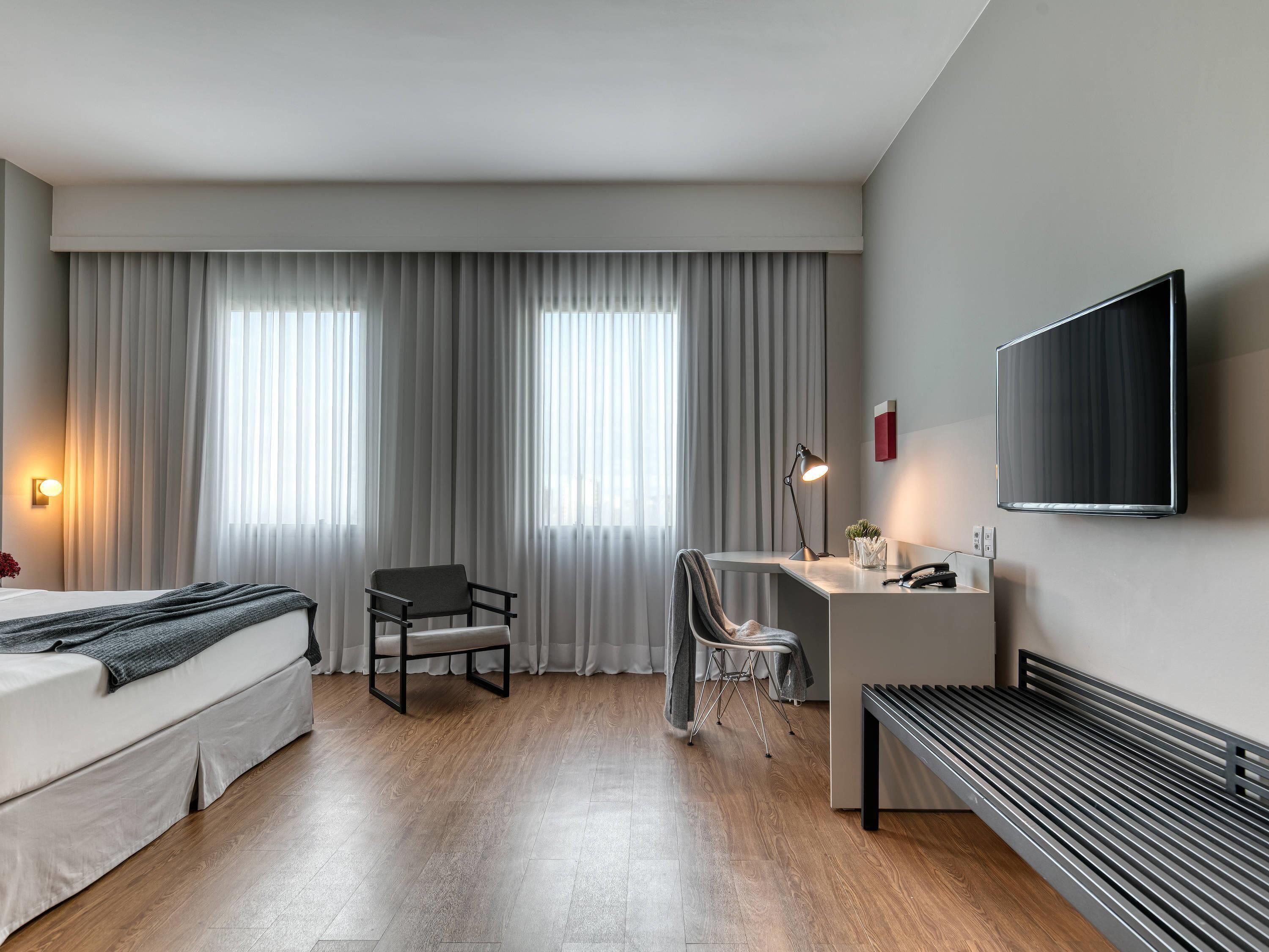 Una habitación de hotel moderna con cama, escritorio, silla y televisor montado en la pared.