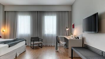 Una habitación de hotel moderna con cama, escritorio, silla y televisor montado en la pared.