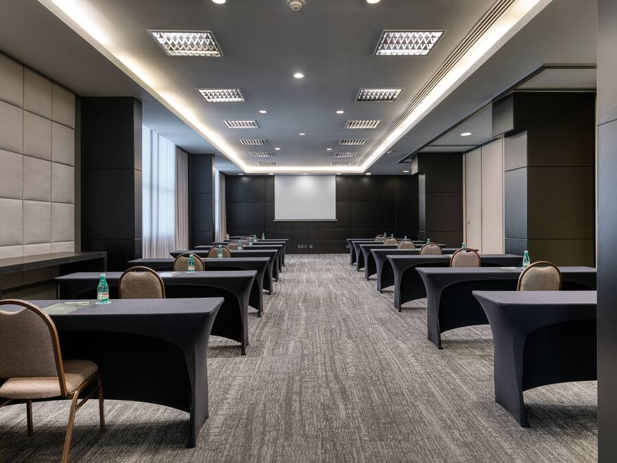 A conference room with multiple tables and chairs, a large screen at the front, and a carpeted floor.
