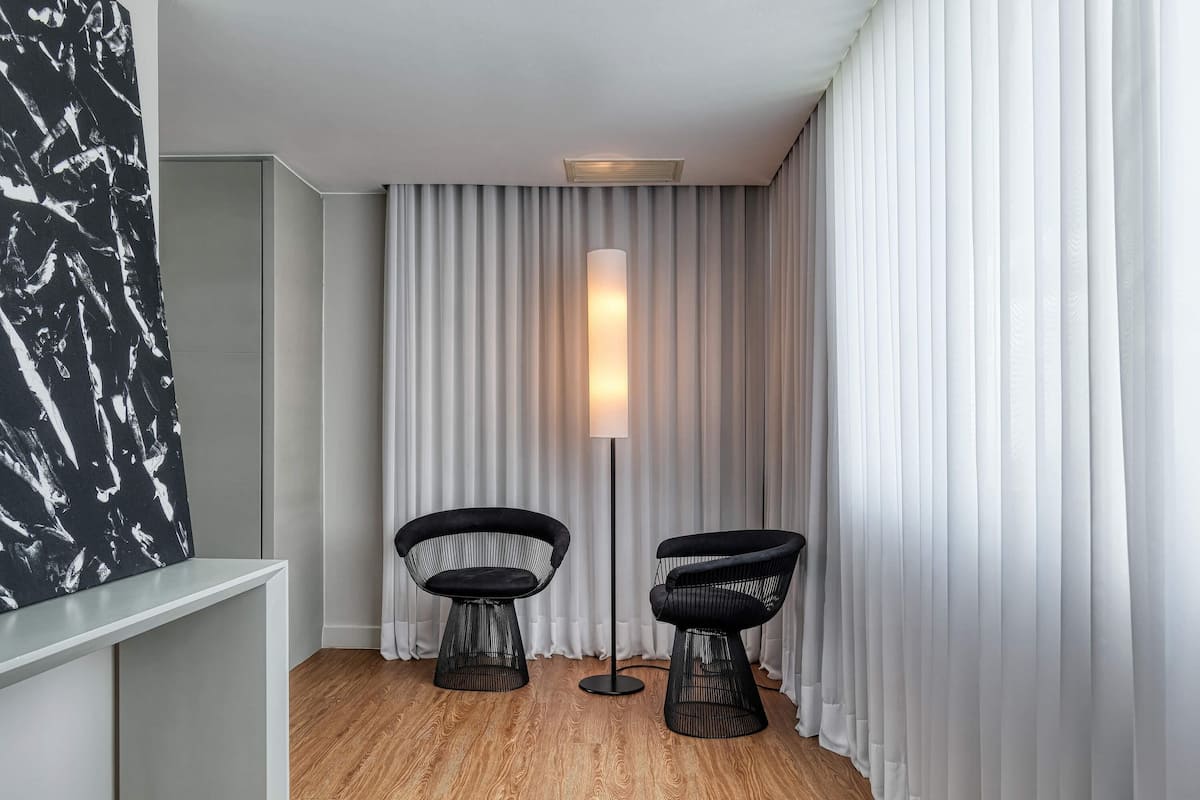 A modern room with a wooden floor, two black chairs, a floor lamp, and a white curtain.
