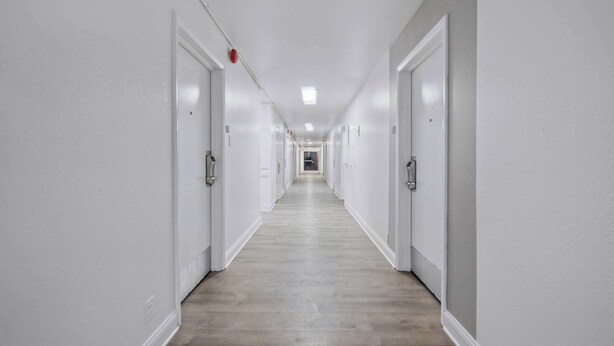 Un long couloir étroit aux murs blancs et au plancher en bois.