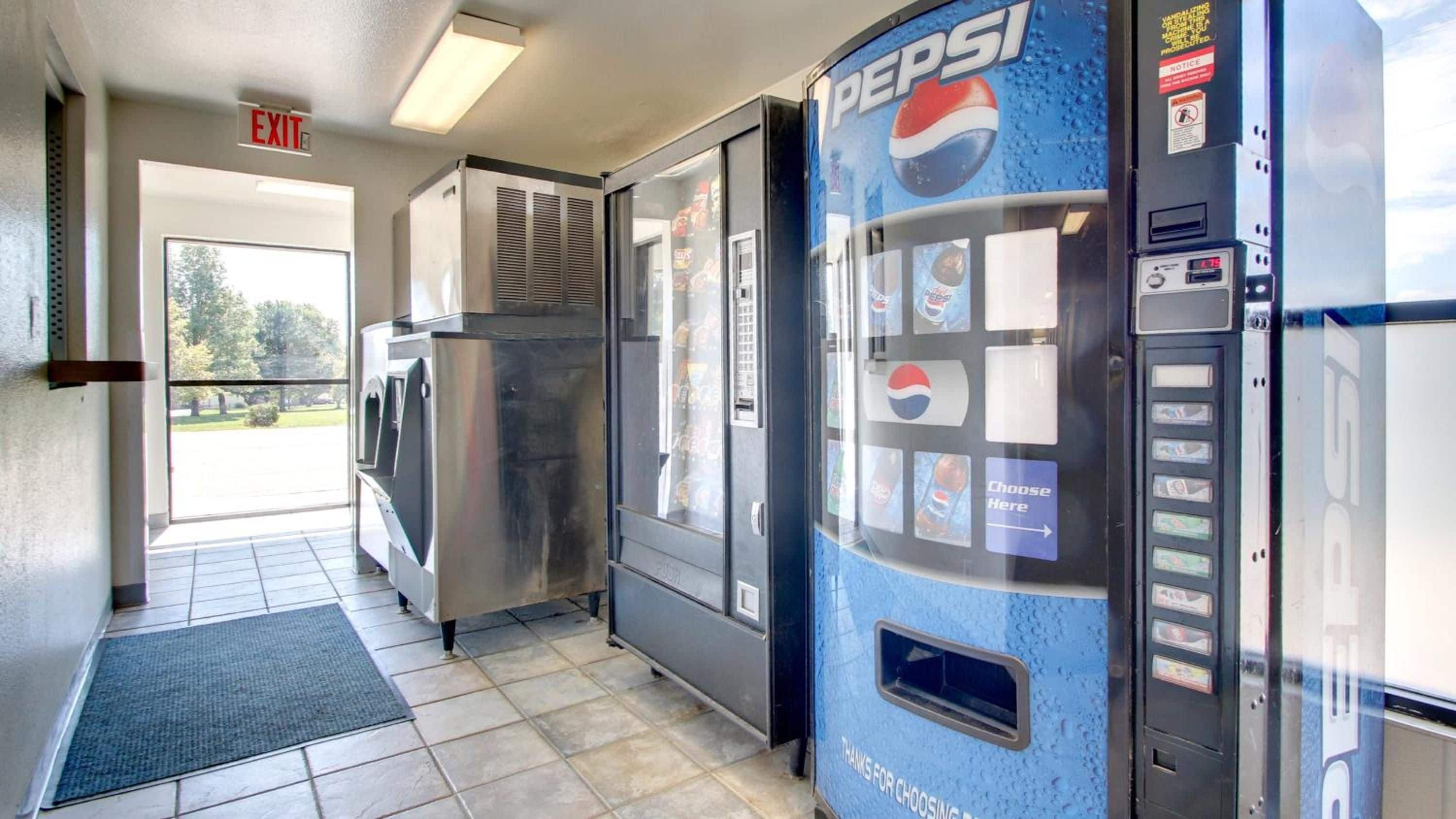 A vending machine area with a Pepsi machine, a refrigerator, and an exit sign.