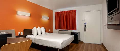 Una habitación de hotel con cama, escritorio, silla, televisor y puerta.