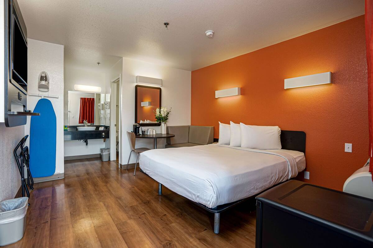 Ein Hotelzimmer mit einem Bett, einem Schreibtisch, einem Sessel, einem kleinen Tisch, einem Spiegel und einem Fernseher.