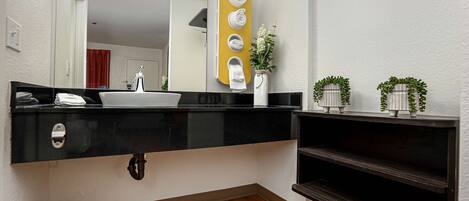 A modern bathroom with a black countertop, a white sink, a mirror, and a towel rack.