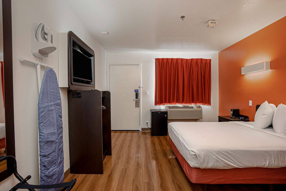 Ein Hotelzimmer mit Bett, Schreibtisch mit Computer, Fernseher, Heizung und einem fenster mit Vorhängen.