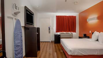 A hotel room with a bed, a desk with a computer, a TV, a heater, and a window with curtains.
