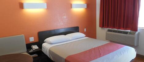 A hotel room with a bed, bedside table, and a desk.