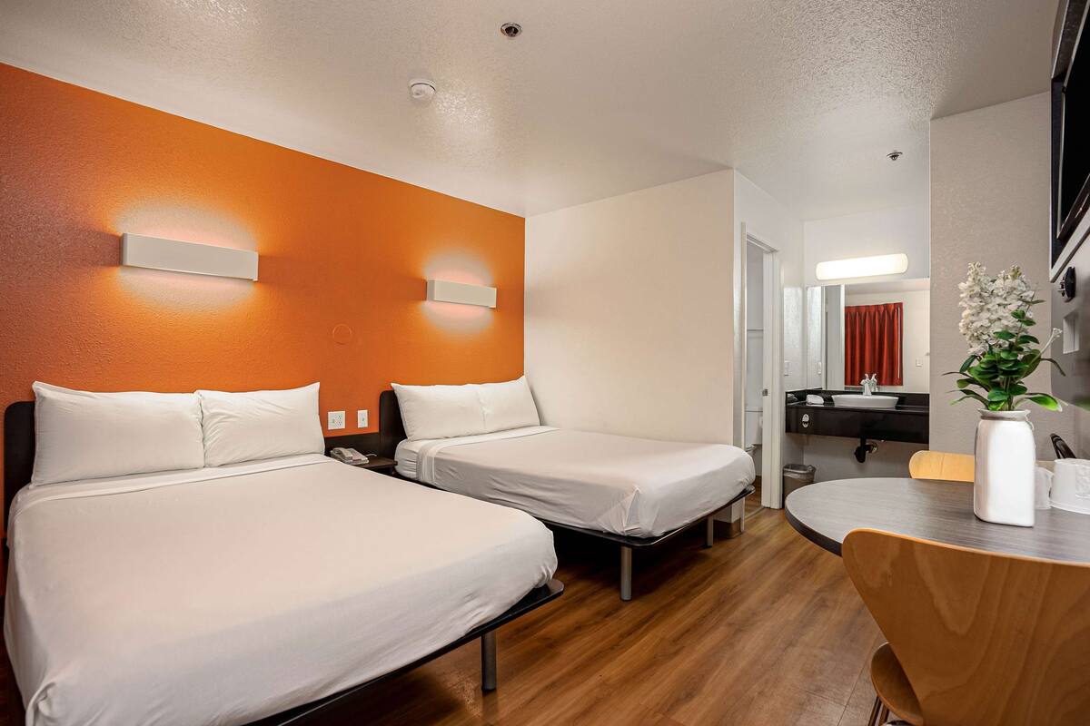 Ein Hotelzimmer mit zwei Einzelbetten, Holzboden, einem runden Esstisch und einem durchgegangenen Tür sichtbaren Badezimmer.