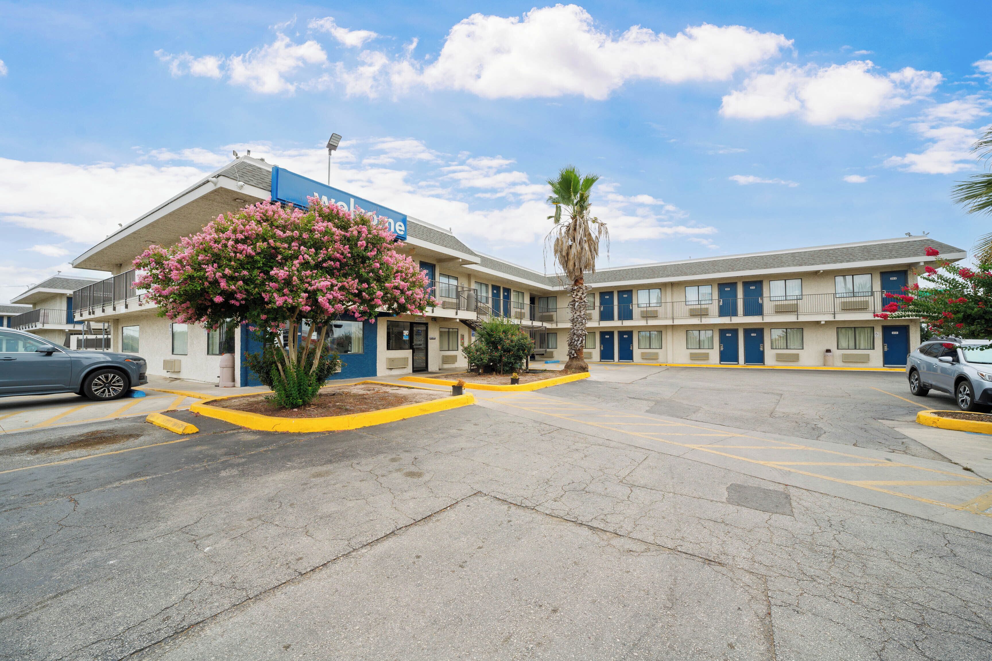 Un motel con estacionamiento, un toldo azul y un árbol de flores rosadas.